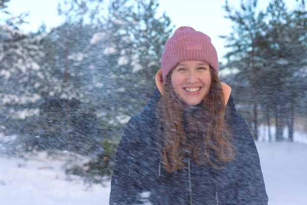 Retrato de uma linda garota fofa no parque ou floresta ao ar livre mulher se divertindo rindo sorrindo para a natureza adolescente em pano quente Blizzard e flocos de neve caindo