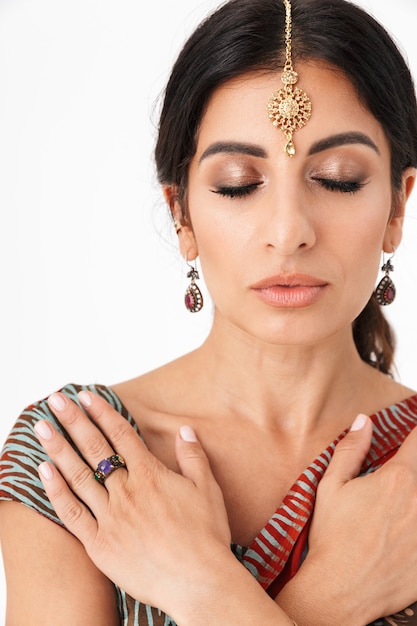 Retrato de uma linda garota hindu usando traje tradicional indiano lehenga choli ou vestido saree e joias étnicas isoladas sobre uma parede branca