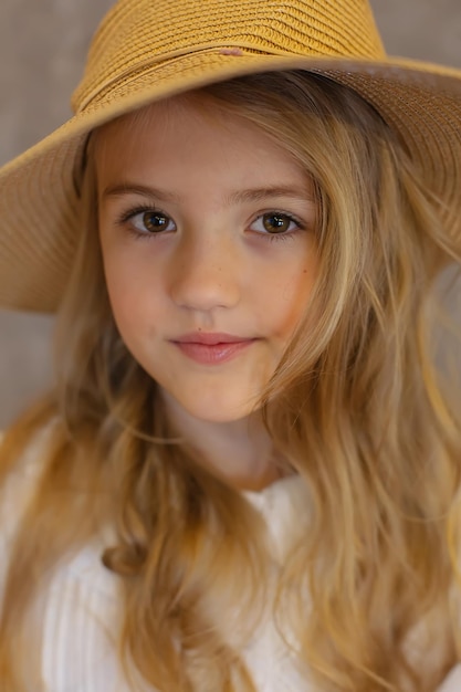 retrato de uma linda garota loira de cabelos compridos em uma blusa branca e um chapéu de palha em um fundo cinza