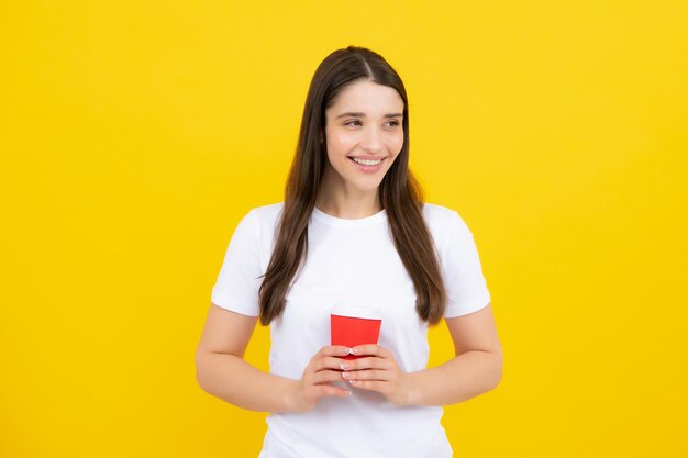 Retrato de uma linda garota segurando uma xícara de café Jovem sorrindo com uma xícara de café isolada em fundo amarelo