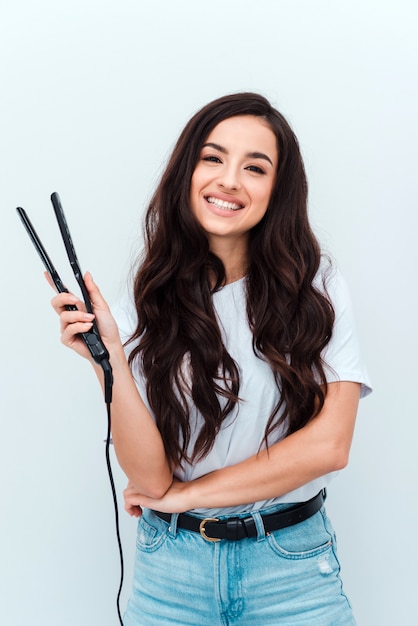 Retrato de uma linda garota usando um alisador de cabelo encaracolado, isolado