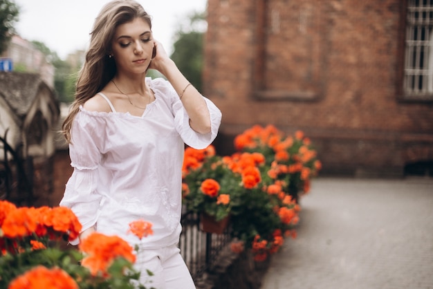 Retrato de uma linda garota vestida de branco e de pé perto das flores