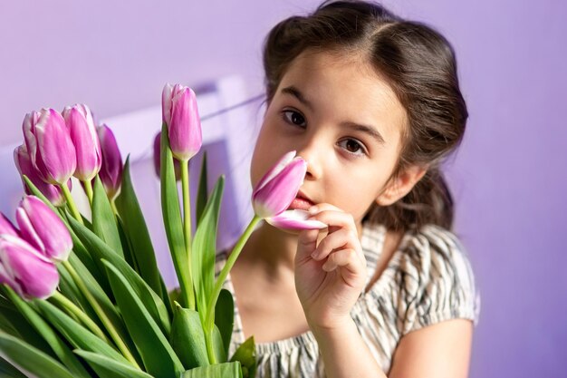 Retrato de uma linda garotinha com um buquê de tulipas olha para o fundo roxo da câmera