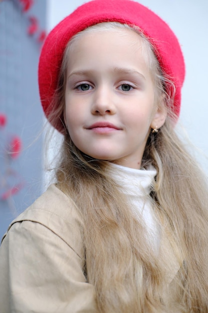 Retrato de uma linda garotinha em um casaco de trincheira e uma boina vermelha que uma garota posa enquanto está sentada em um