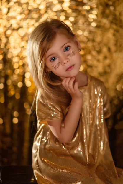 Retrato de uma linda garotinha loira com cabelo comprido em um vestido dourado sobre um fundo dourado bokeh.