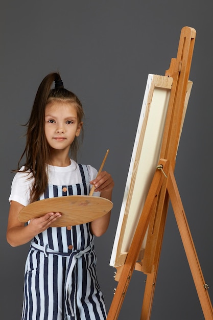 Retrato de uma linda garotinha segurando uma paleta de arte de madeira e pincel no fundo do estúdio