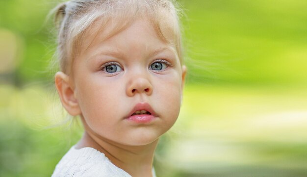 Retrato de uma linda garotinha séria de 2 anos olhando para a câmera no fundo verde desfocado com espaço de cópia