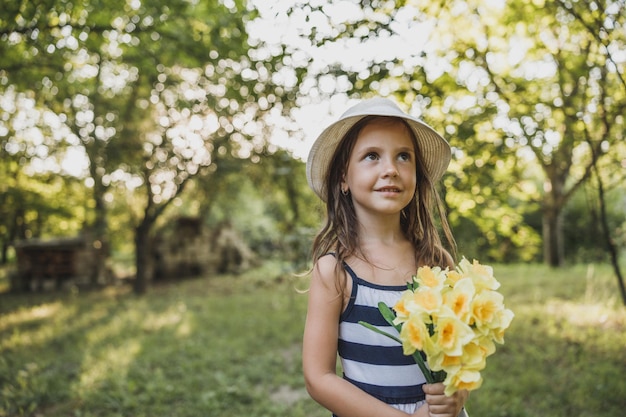 Foto retrato de uma linda garotinha sorridente está segurando um buquê de flores de narcisos amarelos em suas mãos enquanto aproveita o dia na natureza.