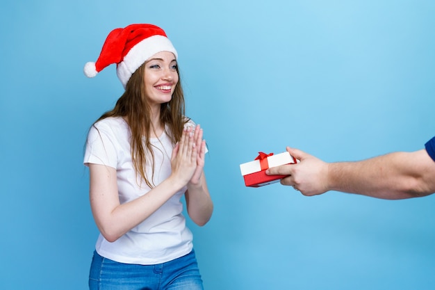 Retrato de uma linda jovem bonita com cabelo comprido, em camiseta branca e chapéu de Papai Noel, recebendo um ...