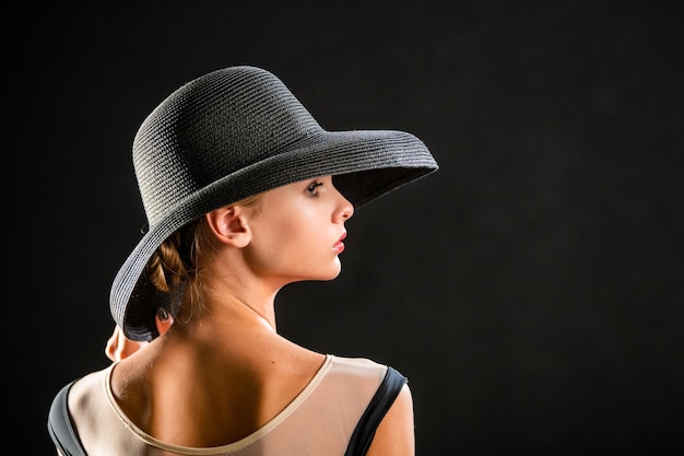 Retrato de uma linda jovem com um elegante chapéu preto em um fundo preto