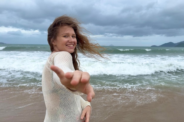 Retrato de uma linda jovem, feliz, alegre, alegre, alegre, aproveitando as férias no mar oceano caminhando na praia de verão em um país tropical sorrindo se divertindo rindo no suéter tricotado