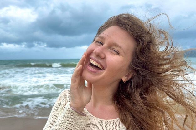 Retrato de uma linda jovem, feliz, alegre, alegre, alegre, aproveitando as férias no mar oceano caminhando na praia de verão em um país tropical sorrindo se divertindo rindo no suéter tricotado