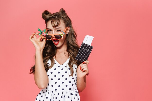 Retrato de uma linda jovem garota pin-up usando um vestido de pé isolado, mostrando o passaporte com a passagem aérea