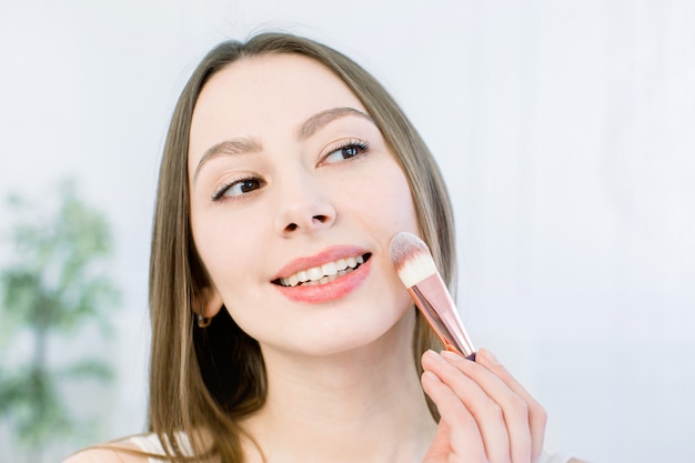 Retrato de uma linda jovem morena com cara limpa. Garota de modelo de spa de beleza com perfeita pele limpa fresca, aplicar escova cosmética.