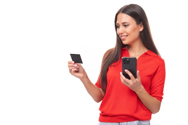 Retrato de uma linda jovem morena europeia em uma camiseta vermelha usando transferências de dinheiro on-line usando um