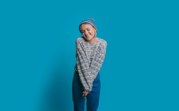 Retrato de uma linda jovem mulher vestida de azul, sorrindo com os olhos fechados feliz isolado na parede azul do estúdio.