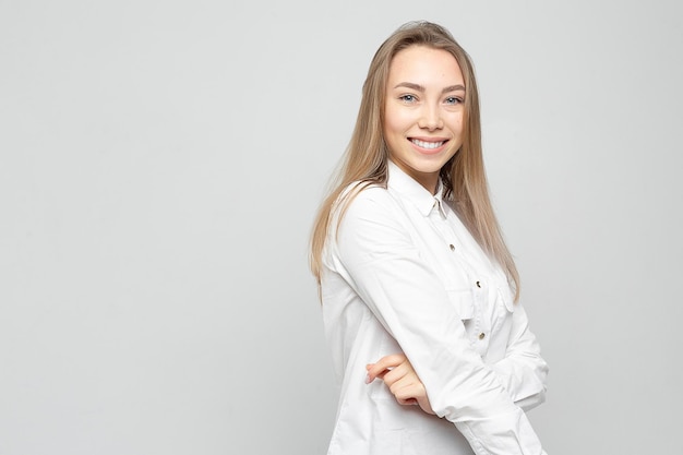 Retrato de uma linda jovem Retrato de uma linda garota loira sorridente em uma camisa branca em um cinza branco