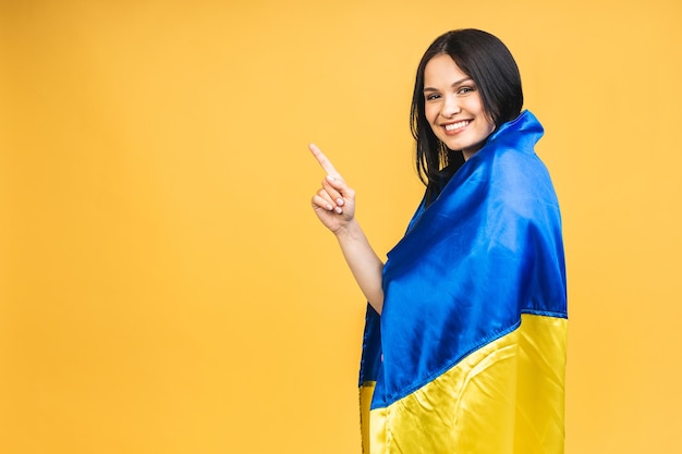 Retrato de uma linda linda e alegre mulher segurando nas mãos a bandeira ucraniana se divertindo isolada sobre fundo amarelo pastel Apontando o dedo