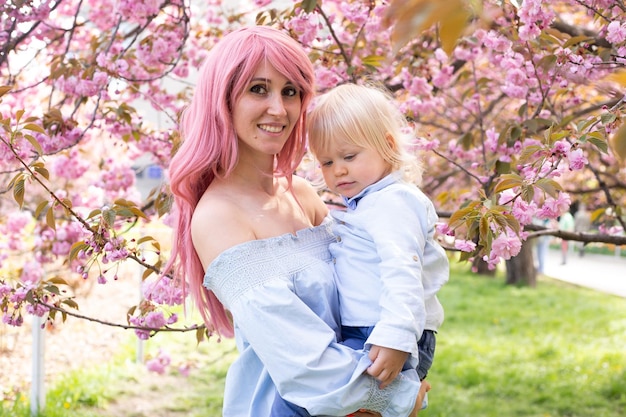 Retrato de uma linda mãe segura em seus braços um filhinho fofo mamãe e garotinho em um jardim florido sakura