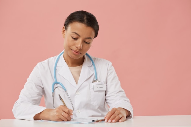 Retrato de uma linda médica escrevendo na área de transferência enquanto preenche papéis