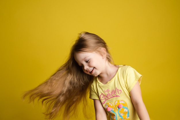 Retrato de uma linda menina com cabelos longos, sorrindo posando isolado no fundo amarelo studio