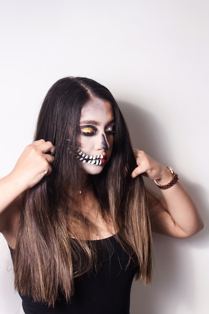 Retrato de uma linda menina com maquiagem de halloween, penteando o cabelo no fundo branco.