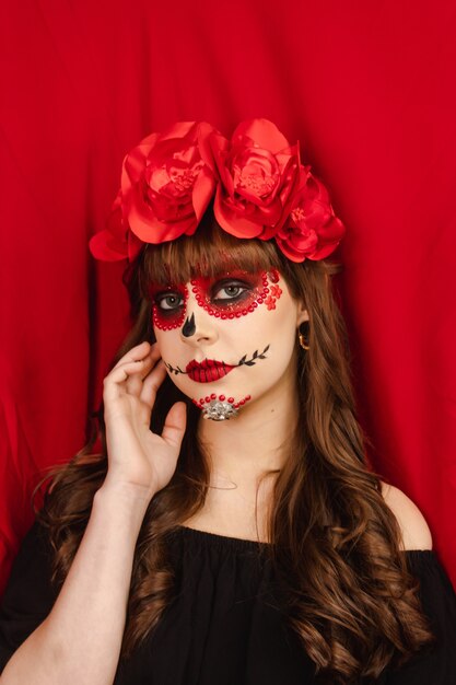 Retrato de uma linda menina com maquiagem Dia de los Muertos com fundo vermelho.