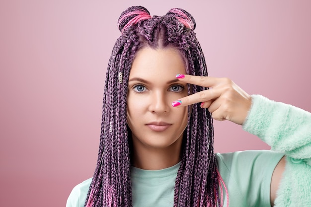 Retrato de uma linda menina com um penteado de tranças cor de rosa com roupas turquesas, posando em um fundo rosa no estúdio. O conceito é estilo moderno, individualidade, abrangência, criatividade.