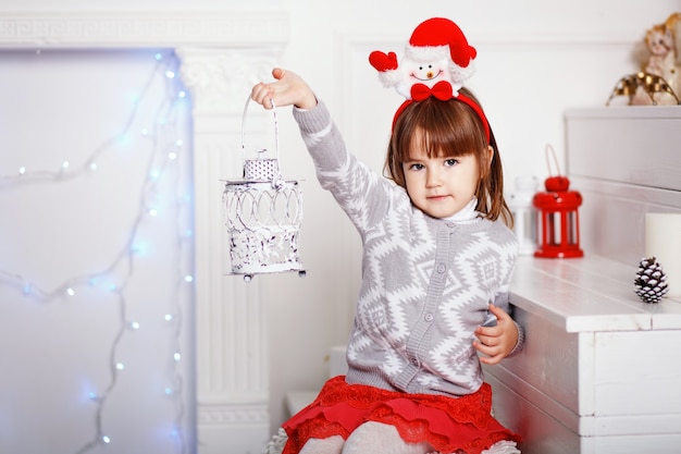 Retrato de uma linda menina com uma faixa decorativa de Natal do Festival de Boneco de neve segurando um castiçal