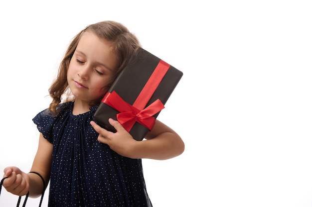 Foto retrato de uma linda menina de 4 anos com os olhos fechados, segurando um presente e um pacote de compras, posando contra um fundo branco com espaço de cópia. conceito de black friday