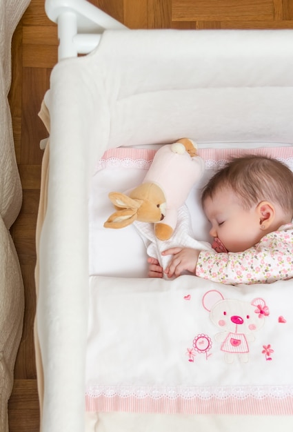 Foto retrato de uma linda menina dormindo em um berço com chupeta e brinquedo de pelúcia