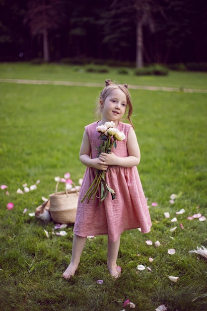 Retrato de uma linda menina em um vestido rosa em pé com um buquê de flores em um prado verde no verão