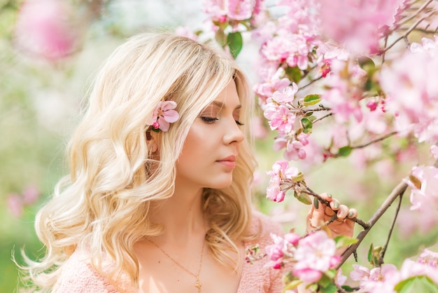 Retrato de uma linda menina loira em um jardim de primavera. Flores de maçã rosa