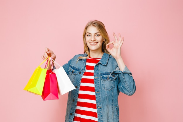 Retrato de uma linda menina loira segurando sacolas de compras e é feliz em um fundo rosa