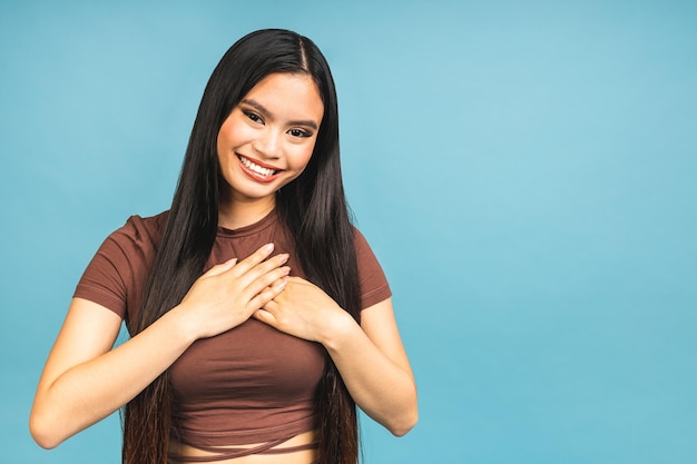 Retrato de uma linda menina morena asiática sorridente, posando isolada sobre fundo azul Jovem mulher está de pé na parede em branco