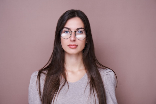 Retrato de uma linda menina morena com óculos e expressão facial séria isolada em parede marrom