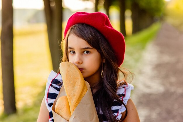 Foto retrato de uma linda menina morena segurando uma baguete francesa