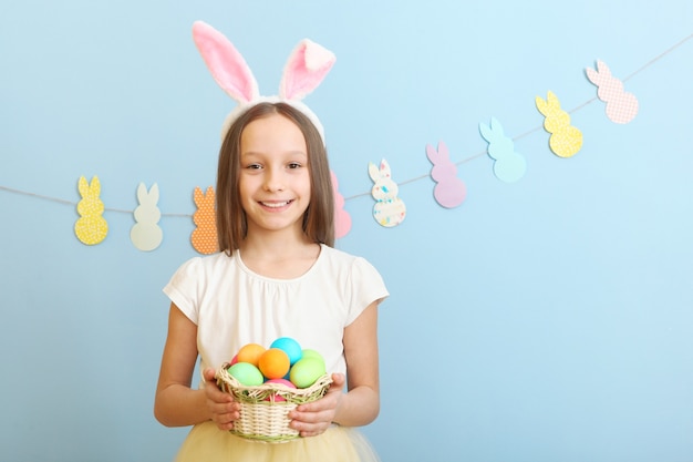 Retrato de uma linda menina sorridente com orelhas de coelho e ovos de Páscoa nas mãos