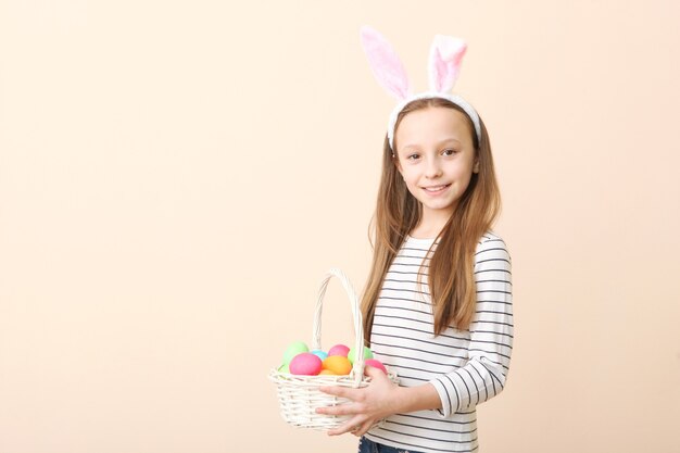Retrato de uma linda menina sorridente com orelhas de coelho e ovos de páscoa nas mãos