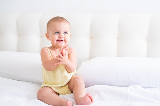 Retrato de uma linda menina sorridente em macacão amarelo na cama branca criança recém-nascida saudável