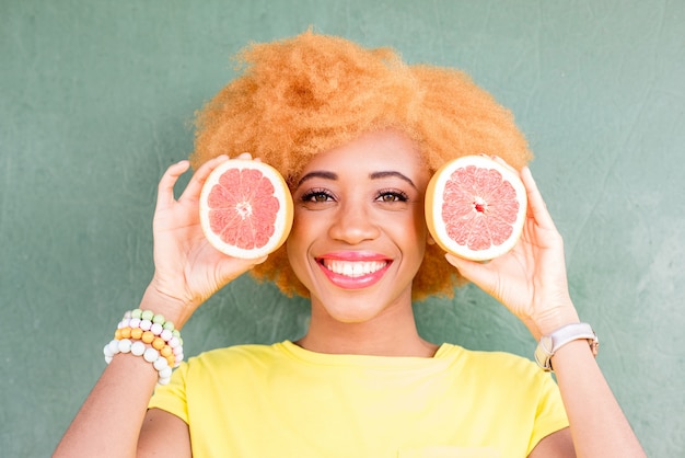 Retrato de uma linda mulher africana com fatias de toranja no fundo da parede verde