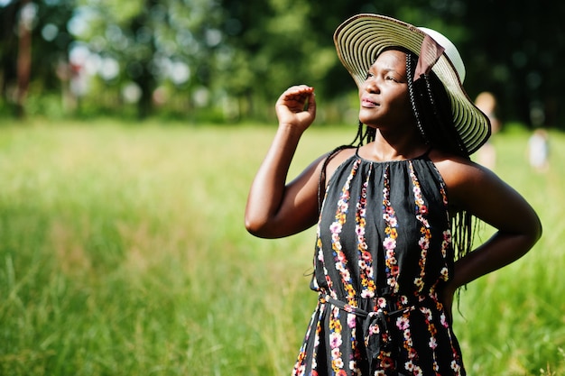 Retrato de uma linda mulher afro-americana de 20 anos no chapéu de verão posando na grama verde no parque.