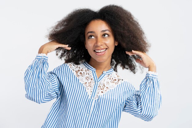 Retrato de uma linda mulher afro-americana positiva, fixando cabelos cacheados, olhando para longe, isolado no fundo branco, conceito de tratamento de procedimentos cosméticos de cuidados com os cabelos