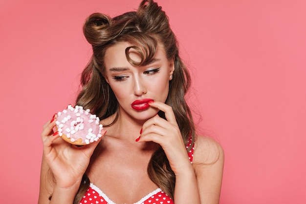 Foto retrato de uma linda mulher alegre de pin-up vestindo maiô, isolada, comendo rosquinha