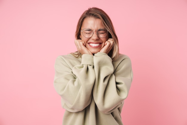 Retrato de uma linda mulher animada em óculos, sorrindo com os olhos fechados, isolados em rosa