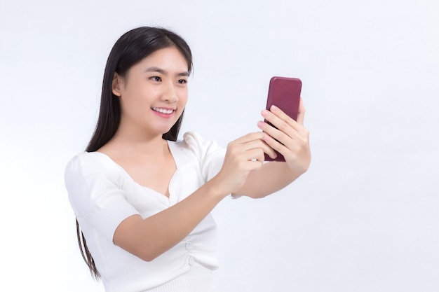 Retrato de uma linda mulher asiática com cabelo comprido preto em uma camisa branca segurando o smartphone