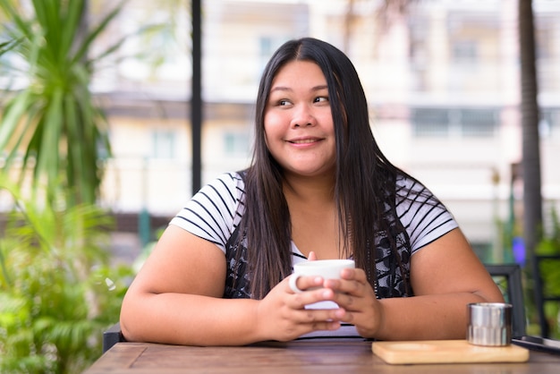 Retrato de uma linda mulher asiática com excesso de peso relaxando em uma cafeteria