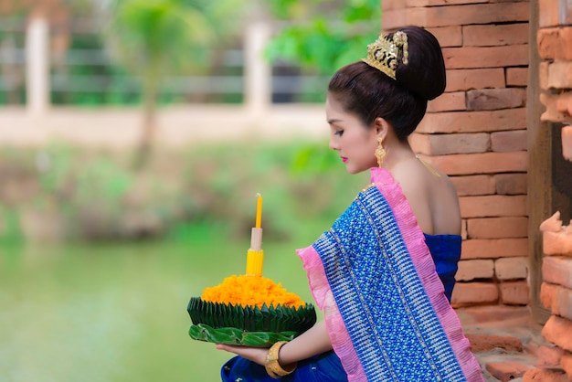 Retrato de uma linda mulher asiática em vestido tailandês tradicional rezando kratong para participar do festival loy kratong na tailândia