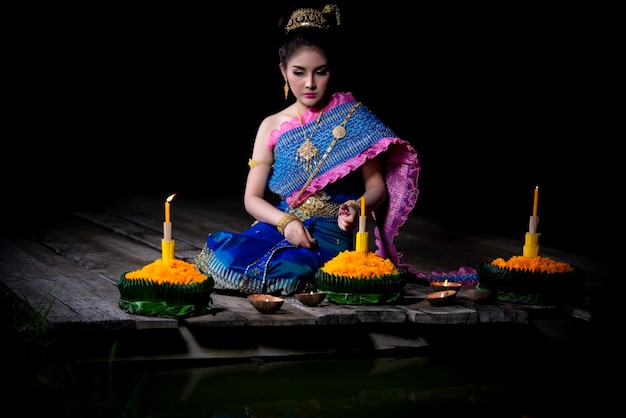 Retrato de uma linda mulher asiática em vestido tailandês tradicional rezando kratong para participar do festival loy kratong na tailândia