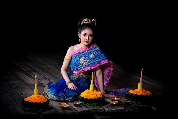 Retrato de uma linda mulher asiática em vestido tailandês tradicional rezando kratong para participar do festival loy kratong na tailândia